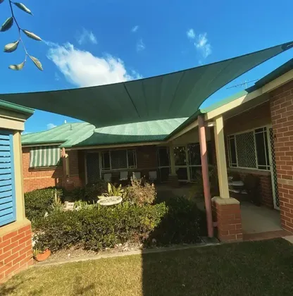 Green shade sail over a brick home patio in Grafton