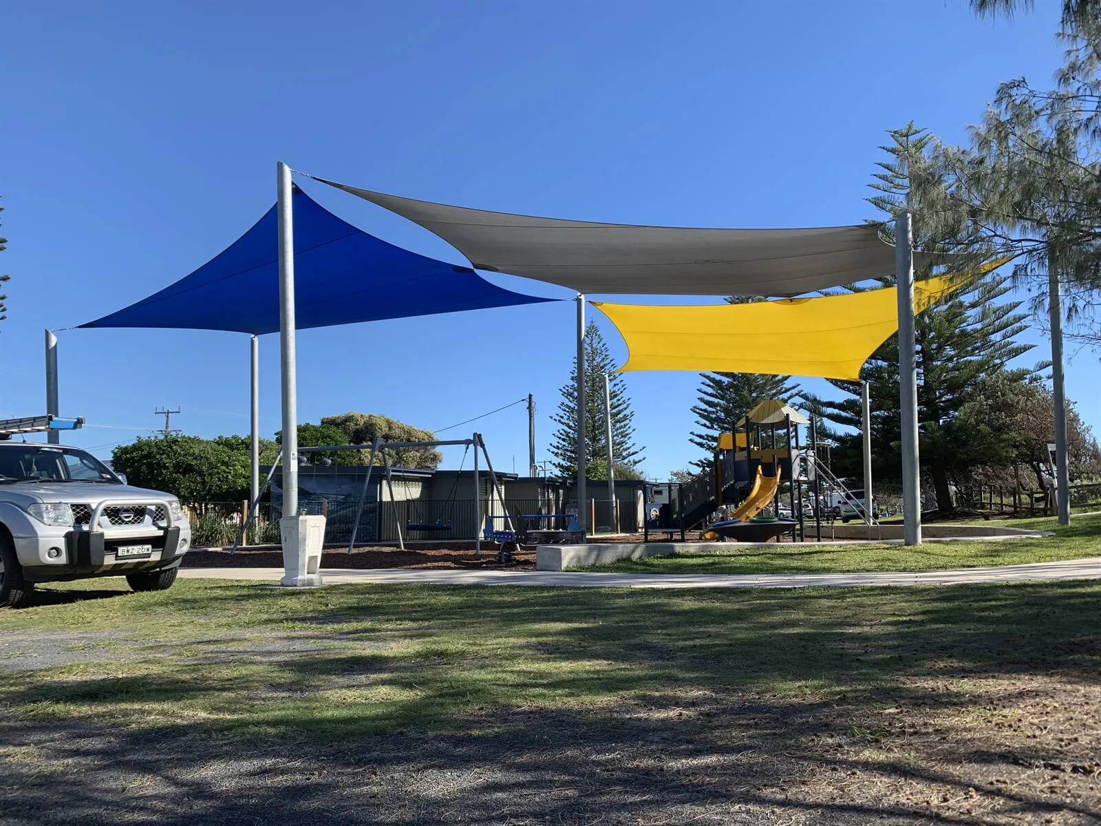 Blue, grey and yellow shade sails over a beachside playground