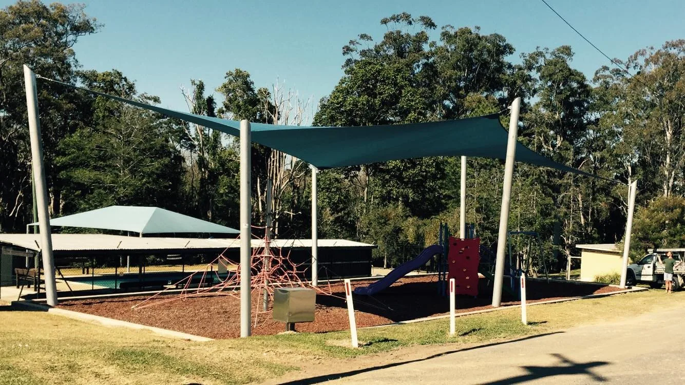 North Coast Shade installer at work on a teal playground sail